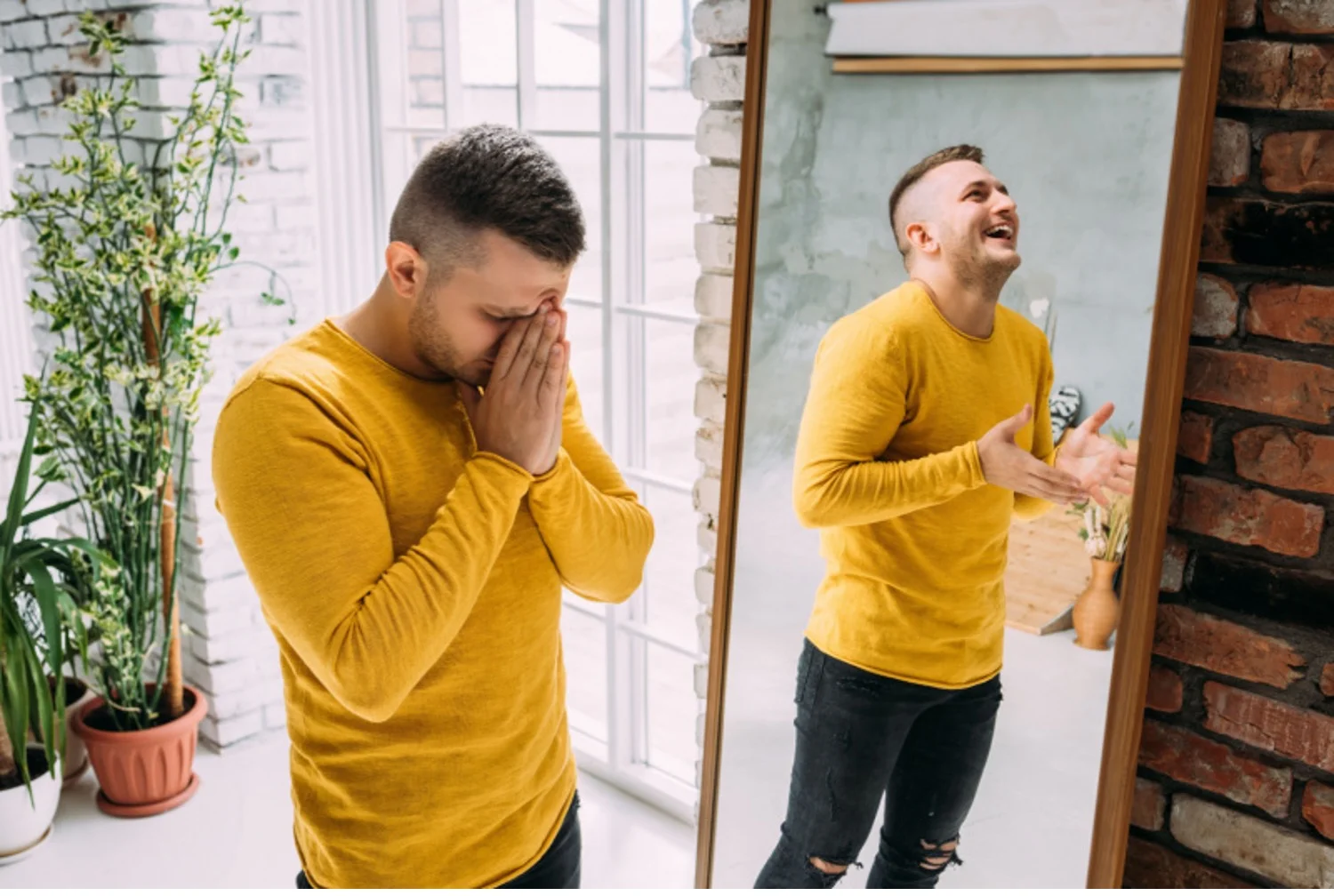 Depressed-looking man with bipolar disorder stands next to a mirror where his reflection shows him in a manic state