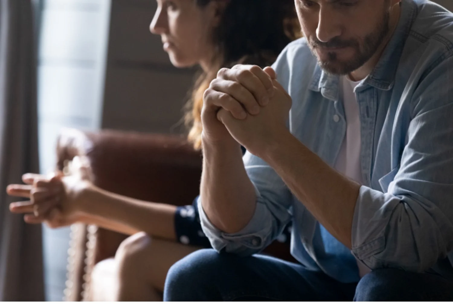 Somber looking couple sits on a couch in a couples therapy session