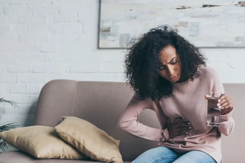 Woman holding a glass of water touches stomach with pained expression on her face