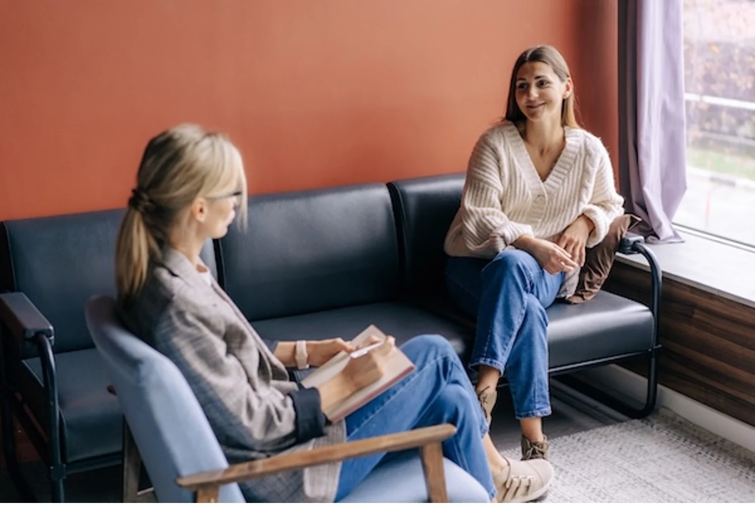 Young smiling woman sits on couch while REBT therapist speaks to her