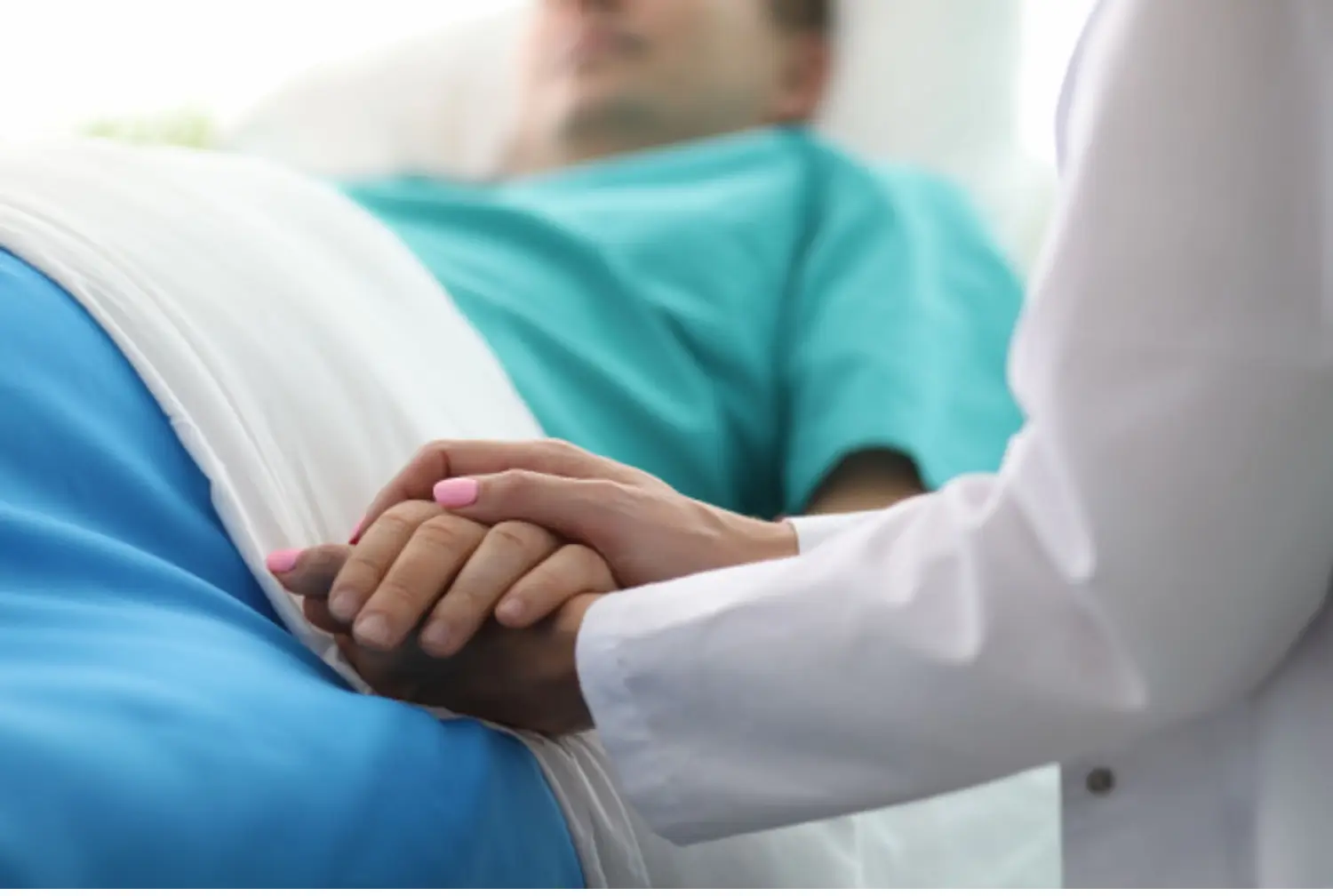 Medical professional holding the hand of a patient in bed during ibogaine treatment