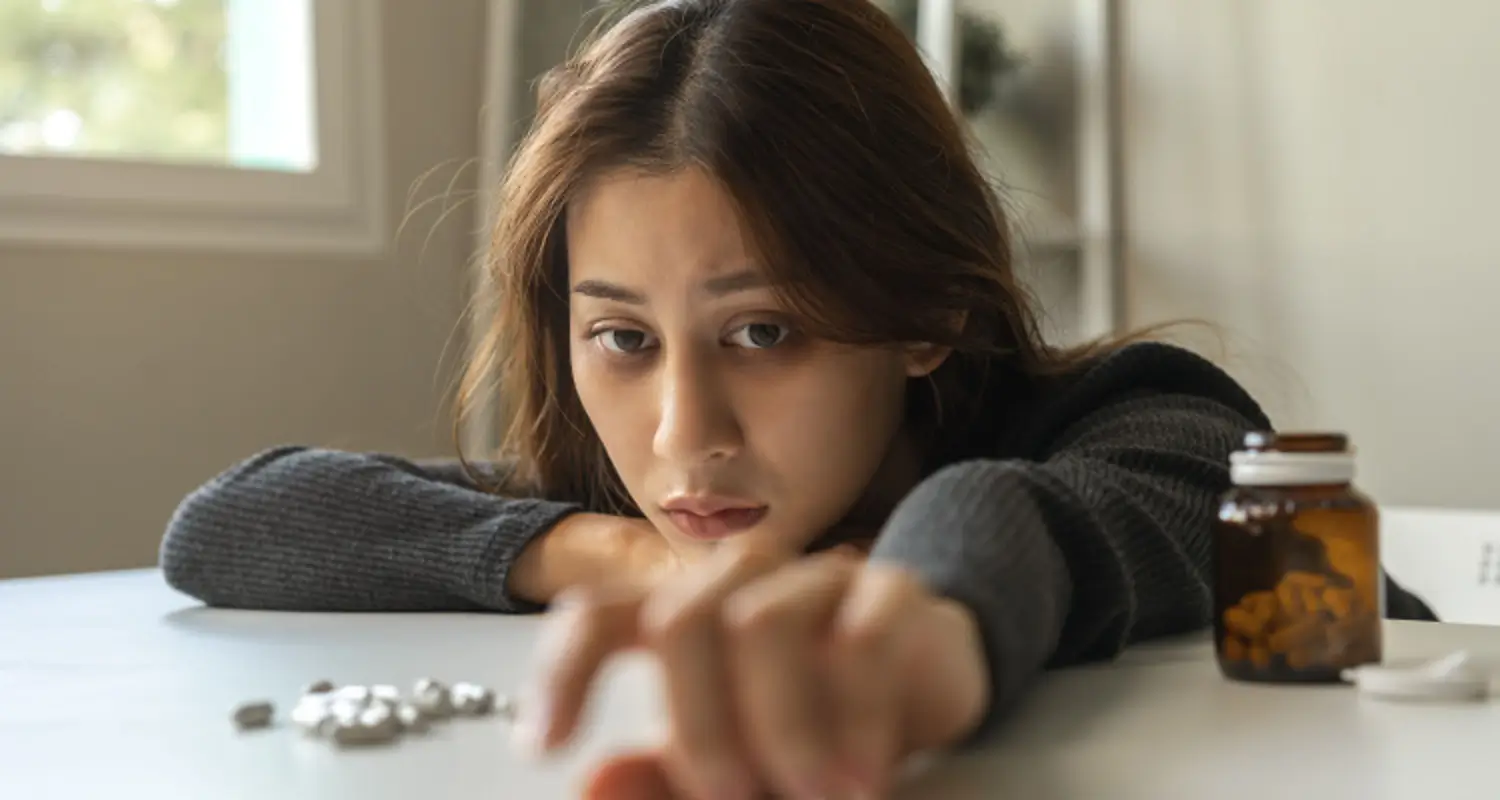 Sick looking woman addicted to pills reaches for a pill on the table